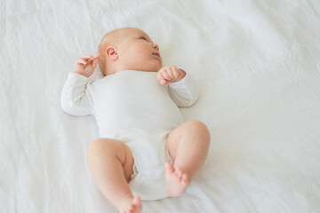 Happy baby. Cute little newborn girl with smiling face lying on bed in bedroom. Infant baby resting...