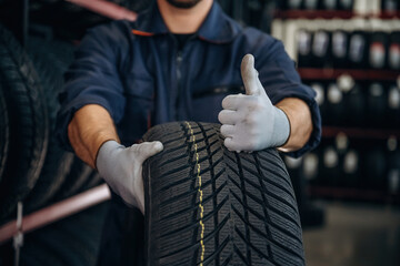 Focused close up view, thumb up, holding a tire. Man worker is maintenance station with wheels © standret