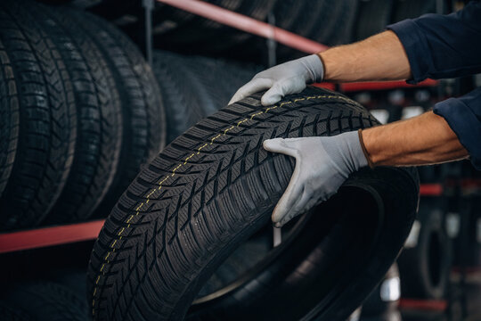 In grey gloves, taking the tire. Man worker is maintenance station with wheels
