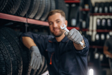 Wrench is in the hand. Man worker is maintenance station with tires, wheels