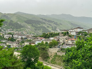 Panoramic view of the city of Gjirokaster, Albania. Nestled in valley between mountains, with a dense cluster of whitewashed houses with traditional layered stone tile roofs. Historical charm. Tourism