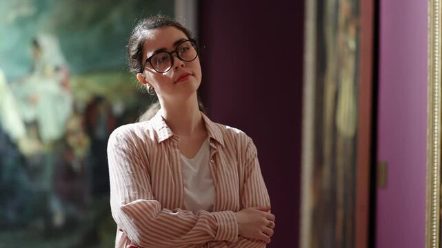 Portrait of a young Caucasian beautiful woman with glasses watching an exhibition of paintings in a gallery. The concept of cultural education.
