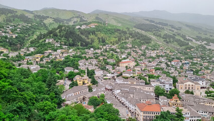 Fototapeta premium Panoramic view of the city of Gjirokaster, Albania. Nestled in valley between mountains, with a dense cluster of whitewashed houses with traditional layered stone tile roofs. Historical charm. Tourism