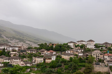 Fototapeta premium Panoramic view of the city of Gjirokaster, Albania. Nestled in valley between mountains, with a dense cluster of whitewashed houses with traditional layered stone tile roofs. Historical charm. Tourism