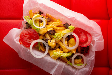 Overhead view of french fries with cheese and meat on red background