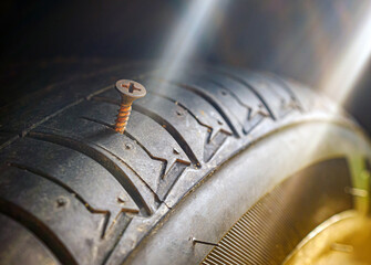 Close-up of a rusty screw driving into a car tire causing a puncture.