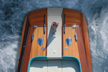 Top view of the back of a luxury, varnished wooden boat for millionaires at sea, moving quickly through the water. The expensive wooden boat leaves a white wake behind as it moves.