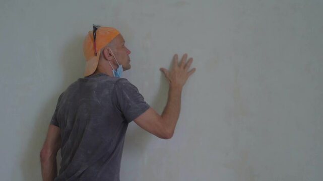 Man builder checking wall after polishing surface for painting. Close-up of a man cleaning and putting putty on a wall, ensuring alignment during apartment repair