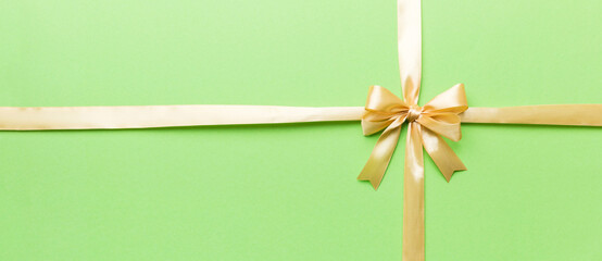 Top view of gold ribbon rolled and yellowbow isolated on colored background. Flat lay with copy space