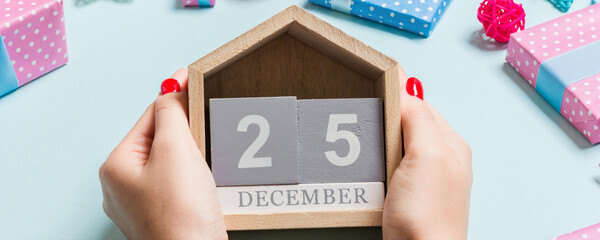 Top view of female hands holding calendar on purple background. The twenty fifth of December. Holiday decorations. Christmas time concept