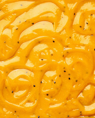 Close-up of a smooth, glossy mixture of passion fruit and mango pulp with visible seeds and texture with swirls ideal for enhancing desserts.. Bakery sweets concept.