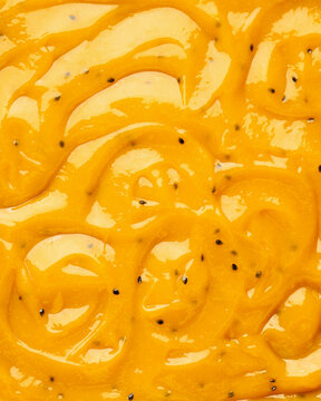 Close-up of a smooth, glossy mixture of passion fruit and mango pulp with visible seeds and texture with swirls ideal for enhancing desserts.. Bakery sweets concept.