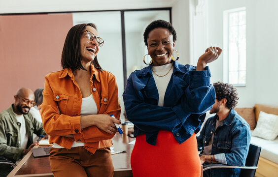 Young women colleagues laughing and enjoying a vibrant and colorful workplace in a creative boardroom