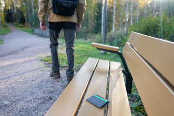 man is leaving from a bench where he lost his credit card holder. Forgotten credit card holder on a...