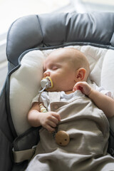Adorable baby sleeps peacefully in crib curled cozily. Newborn baby rests with pacifier in mouth. Childhood.