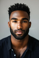 Obraz premium Headshot of a Black mixed race male model with short hair and a beard, wearing a dark shirt on a light background