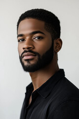 Obraz premium Headshot of a Black mixed race male model with short hair and a beard, wearing a dark shirt on a light background