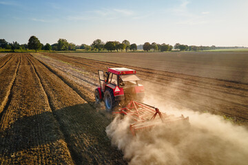 Red tractor working in agricultural field, cultivating and plowing dry soil, aerial view. Agribusiness concept. Small farming concept © Lazy_Bear