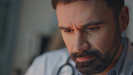 Portrait doctor examining information during night shift. Pensive bearded man