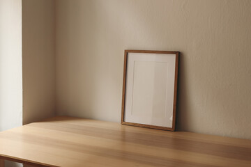 Vertical wooden picture frame, empty poster mockup on wooden table. No content in the frame. Beige wall background. Modern moody minimal interior decor. Side view, copy space, no people.