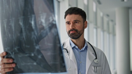 Serious professional examining x-ray in hospital corridor. Closeup doctor work