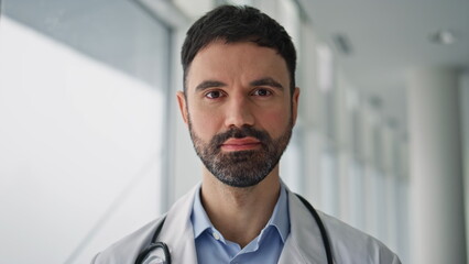 Closeup bearded doctor posing in hospital ward. Smiling professional standing