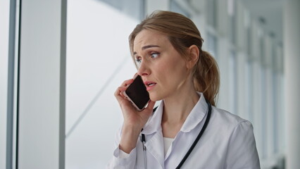 Worried practitioner talking smartphone in hospital closeup. Stressed doctor