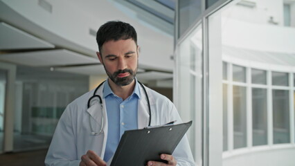 Happy professional going hospital corridor closeup. Bearded man reviewing chart