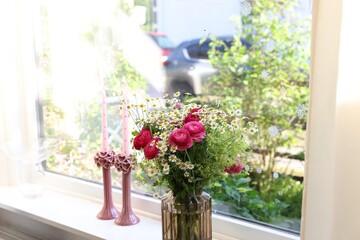 Beautiful ranunculus flowers and chamomiles in vase on windowsill indoors