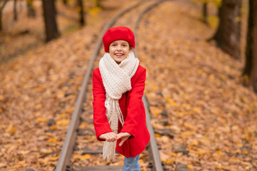 Caucasian girl in a red coat and beret walks along the railway tracks in the park in autumn.