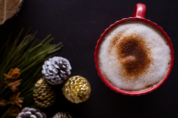 Christmas time, festive cappuccino in red mug with pinecones and greenery on table