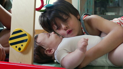 Young boy lying next to a baby on the floor, showing affection and bonding as he gently interacts...