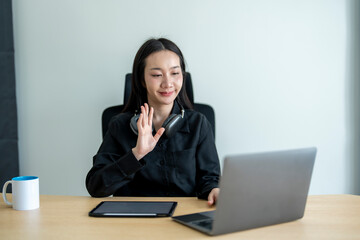 Asian businesswoman waving during video call on laptop at office desk