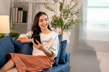 Young woman relaxing on sofa using smartphone at home