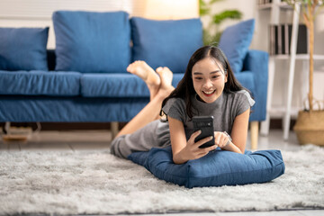 Obraz premium Young woman relaxing at home using smartphone while lying on carpet
