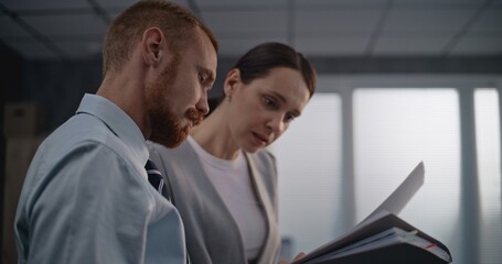 Portrait of two financial specialists or professional bank employees watching documents, discussing project ideas, brainstorming company strategy. Male and female colleagues working in modern office.