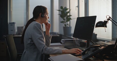 In stylish modern office: Female financial trader in headset works on computer, talks to business...