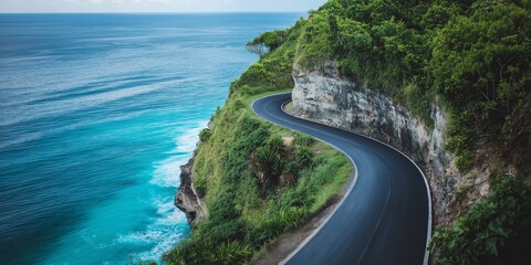 A winding road with a beautiful ocean view in the background. The road is surrounded by lush green trees and the water is calm and blue. The scene is peaceful and serene