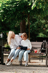 Fototapeta premium Information in notepad, reading it. Little schoolgirl with her mother are sitting on the bench outdoors