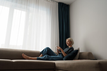 A young woman lounging comfortably on a sofa while using her smartphone. The scene exudes a sense of relaxation and leisure in a cozy home environment.