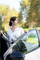 Woman standing by car in sunlit park