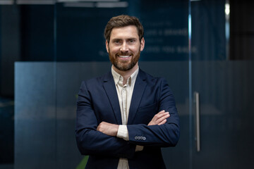 Portrait of a sleepy young businessman standing in the office, arms crossed on his chest,...