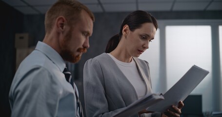Portrait of two financial specialists or professional bank employees watching documents, discussing project ideas, brainstorming company strategy. Male and female colleagues working in modern office.