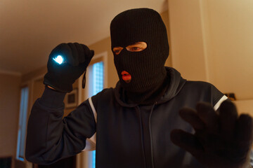 Masked burglar searching home at night using flashlight