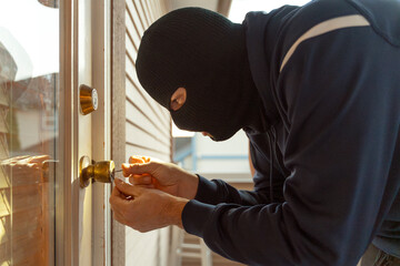 Masked burglar picking lock of front door