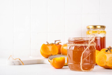Persimmon jam. Sweet autumn homemade jam or marmalade canning preserves in a jar, with whole and cut persimmon c in the background