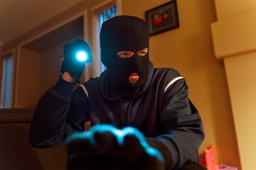 Masked burglar searching for valuables in living room