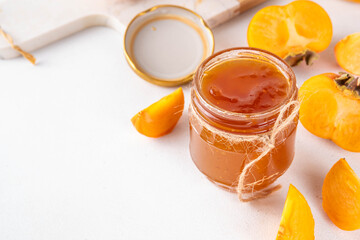 Persimmon jam. Sweet autumn homemade jam or marmalade canning preserves in a jar, with whole and cut persimmon c in the background