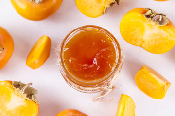 Persimmon jam. Sweet autumn homemade jam or marmalade canning preserves in a jar, with whole and cut persimmon c in the background