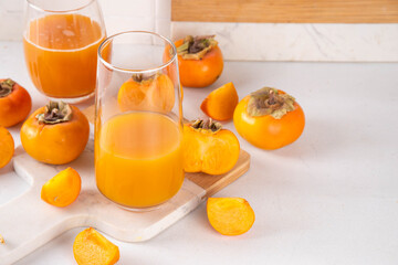 Fresh homemade persimmon juice in portioned glasses, with whole and cut persimmon c in the background